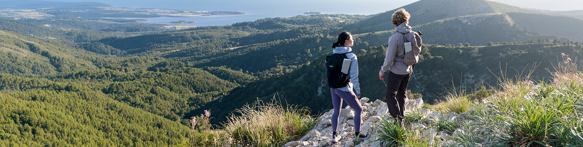 Due escursionisti con zaini guardano colline boscose e il mare